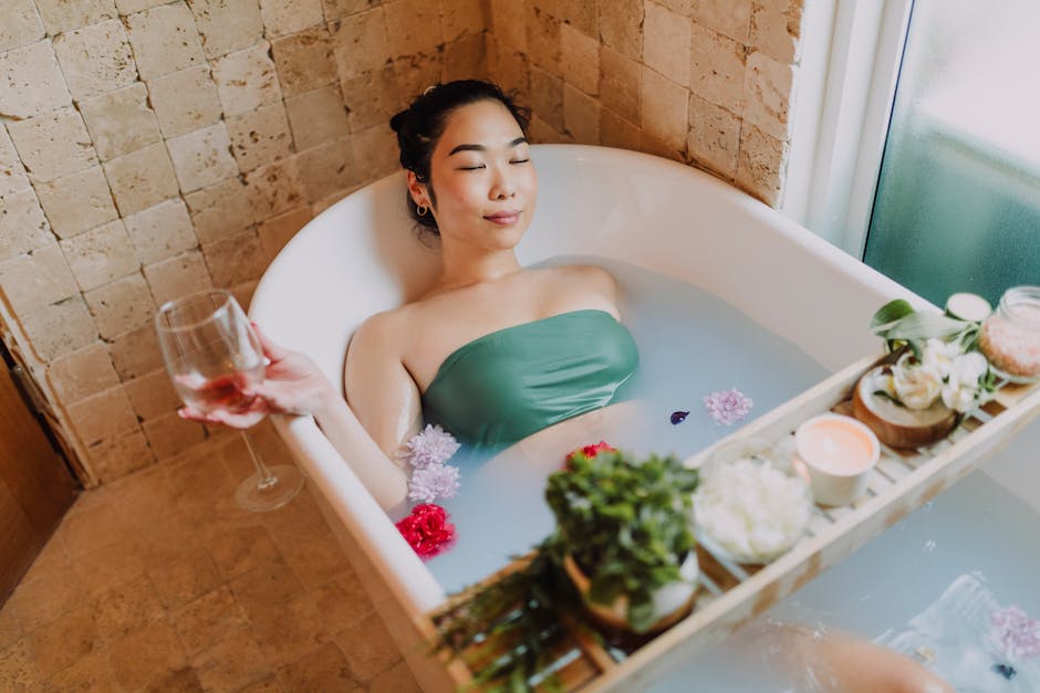Asian woman enjoys a peaceful flower bath, holding a glass of wine, surrounded by candles for a serene spa experience